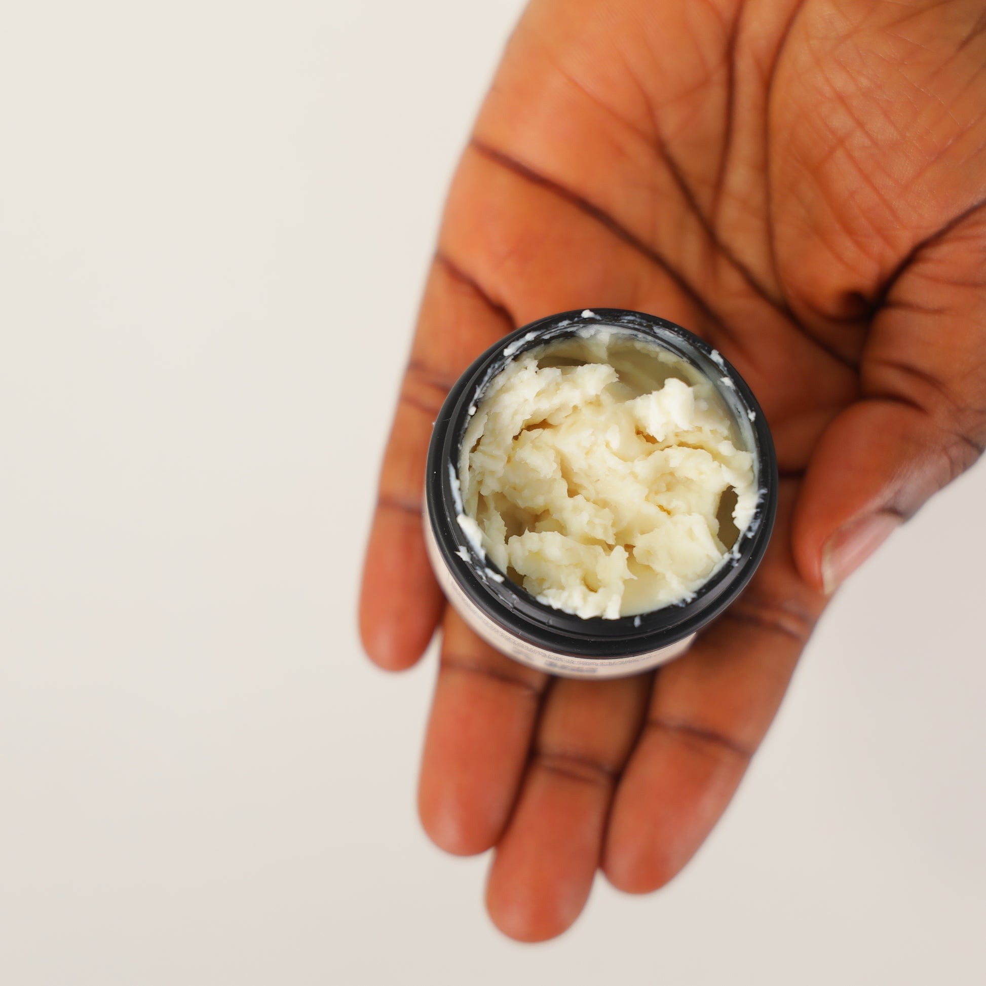 Hand holding a small container of Stori of Africa Body Butter against a plain background