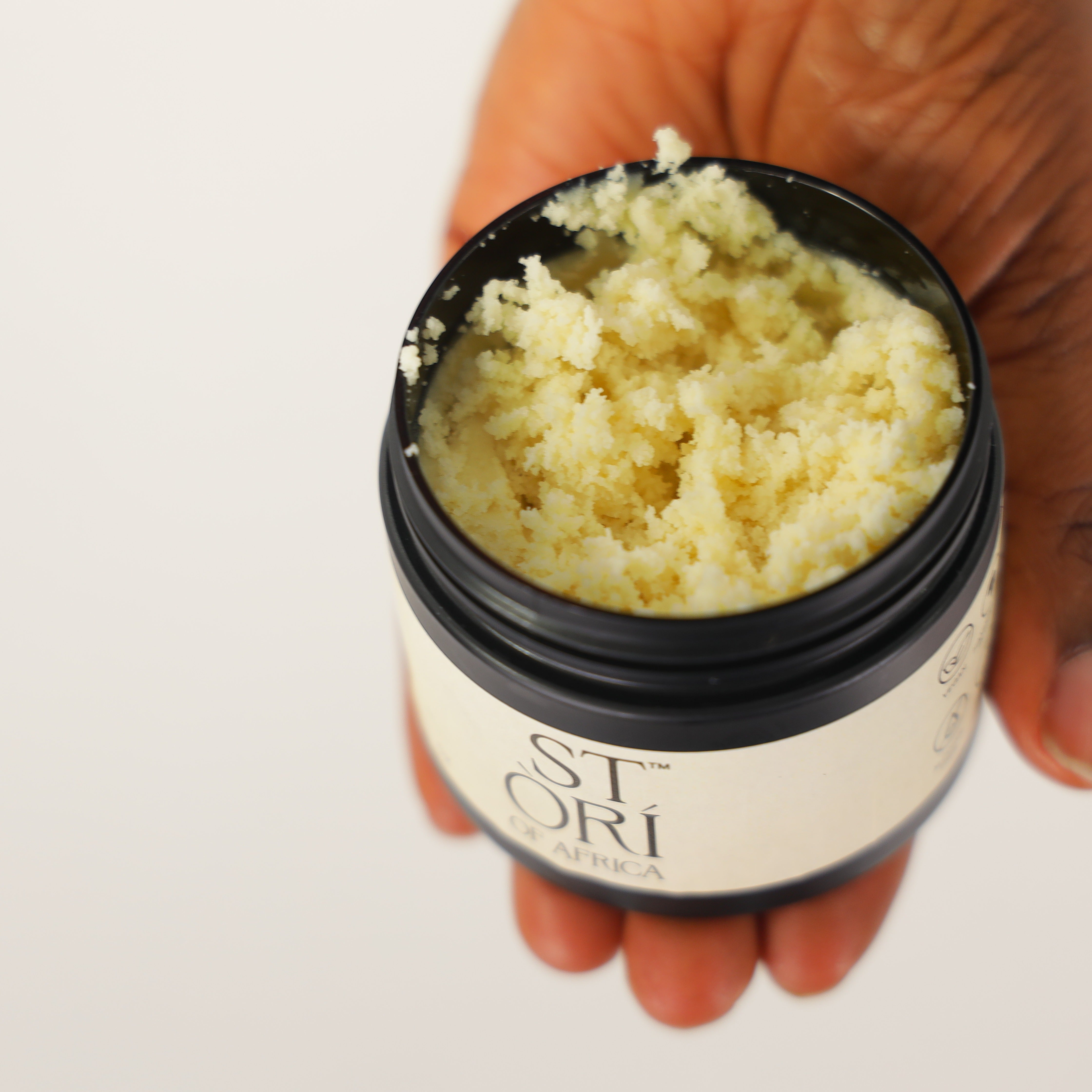 Hand holding a 150ml Jar of Stori of Africa ORI Shea Butter against a plain back